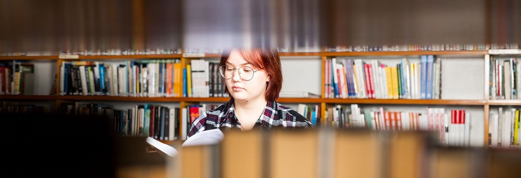 Opiskelijaa lukee selailee kirjaa kirjastossa